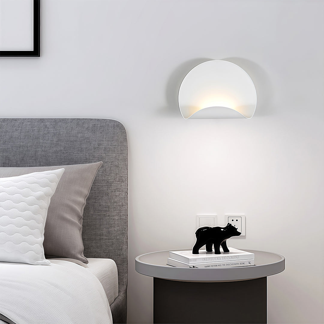 Modern half-moon white wall lights fixture providing soft accent lighting above a gray upholstered headboard and round side table.