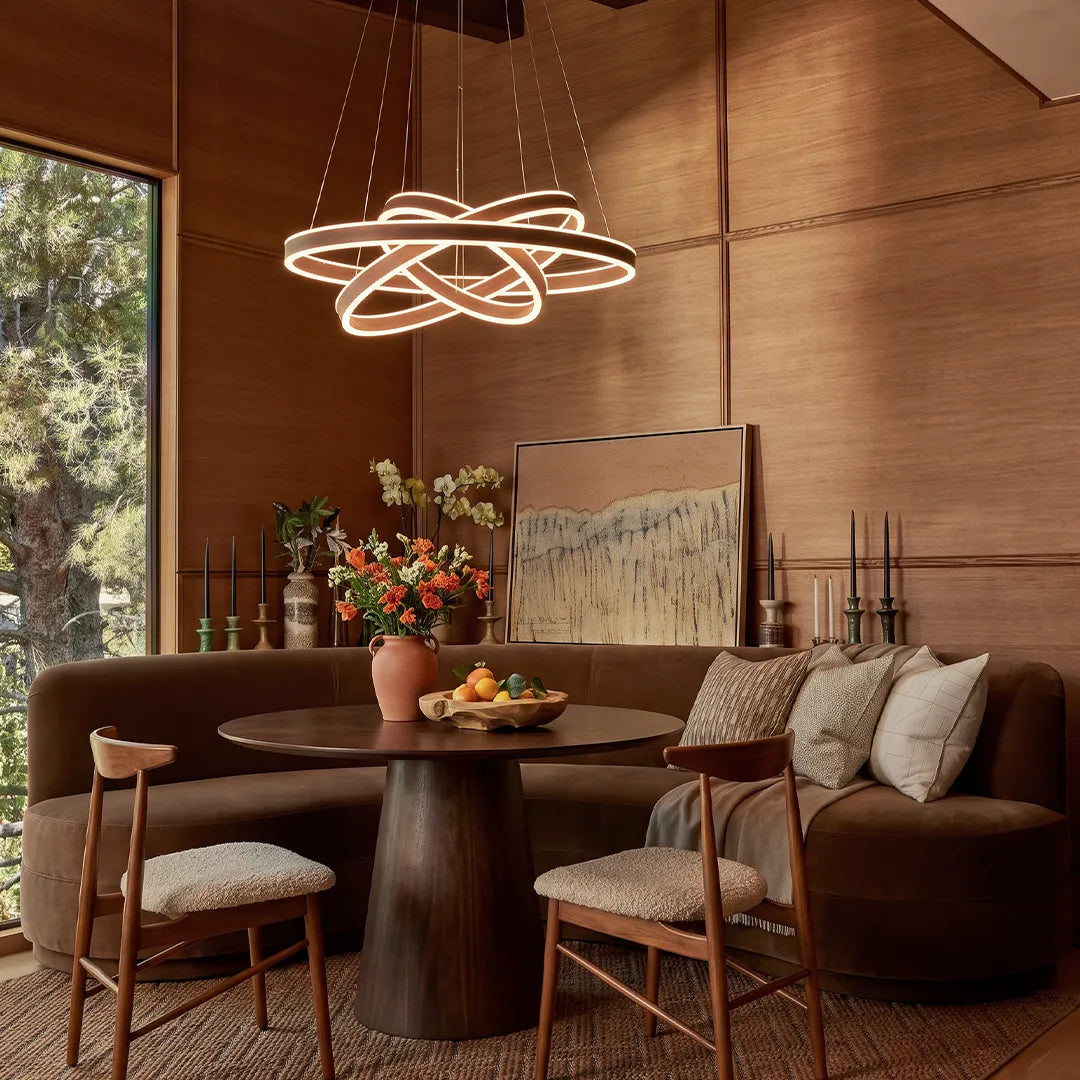 Modern halo chandelier with intertwined LED rings hanging above a round dining table in a warm contemporary interior.