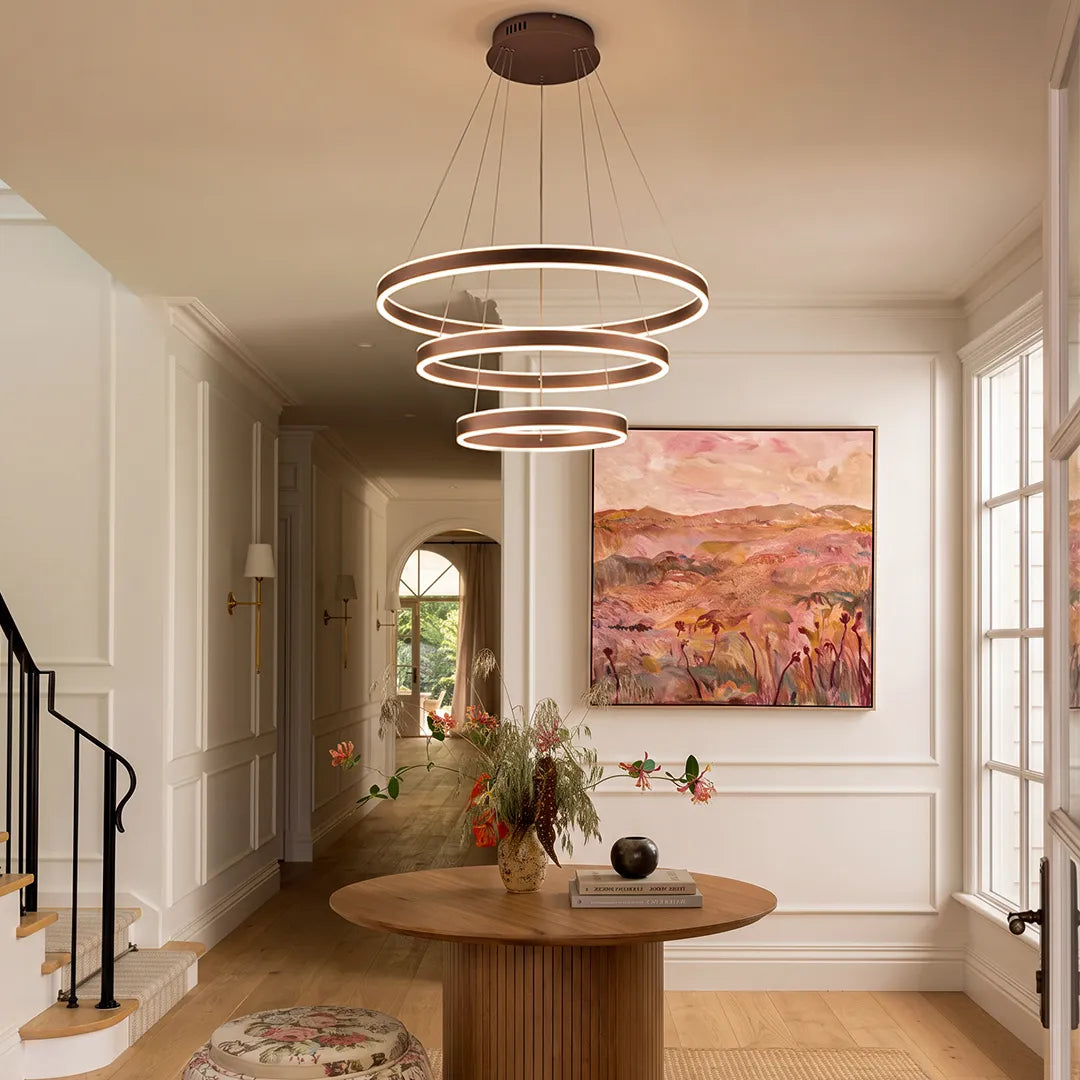 Modern halo chandelier with three suspended LED rings lighting a bright entry hallway with a round table.