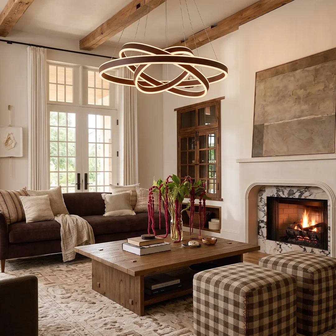Modern halo chandelier with sculptural interlocking LED rings hanging above a cozy living room with exposed beams.
