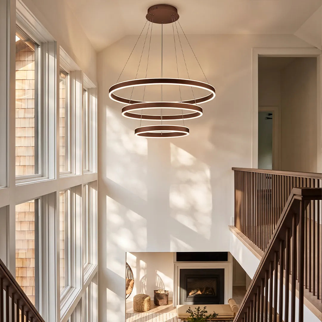 Modern halo chandelier with layered circular LED rings illuminating a tall stairwell and fireplace sitting area.