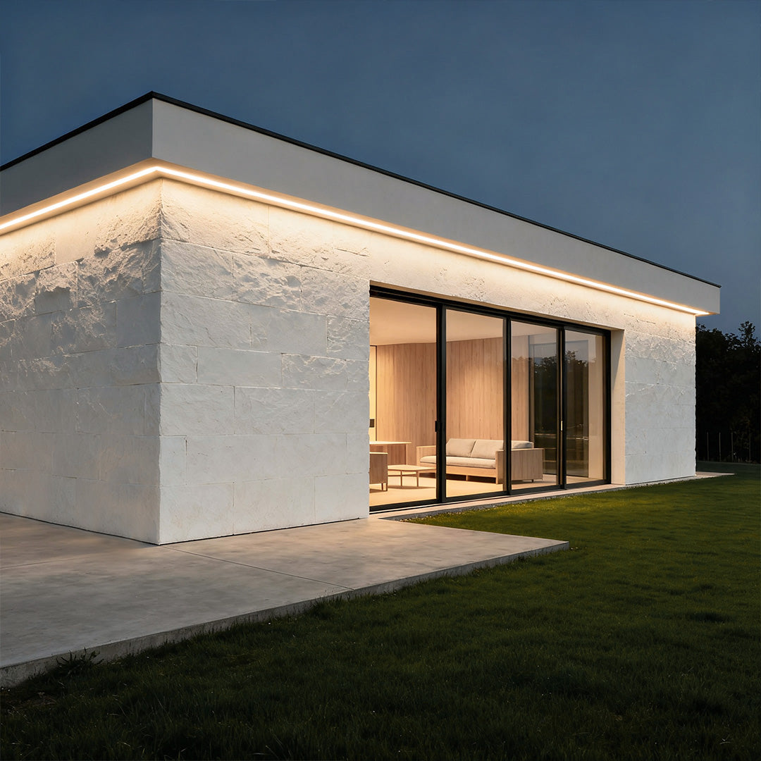Modern house exterior illuminated by linear facade wall washer lights at night.