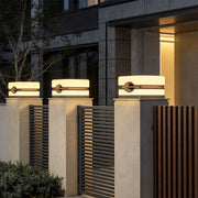 Modern house pillar lights installed along a sleek metal fence with stone pillars at a residential entrance.