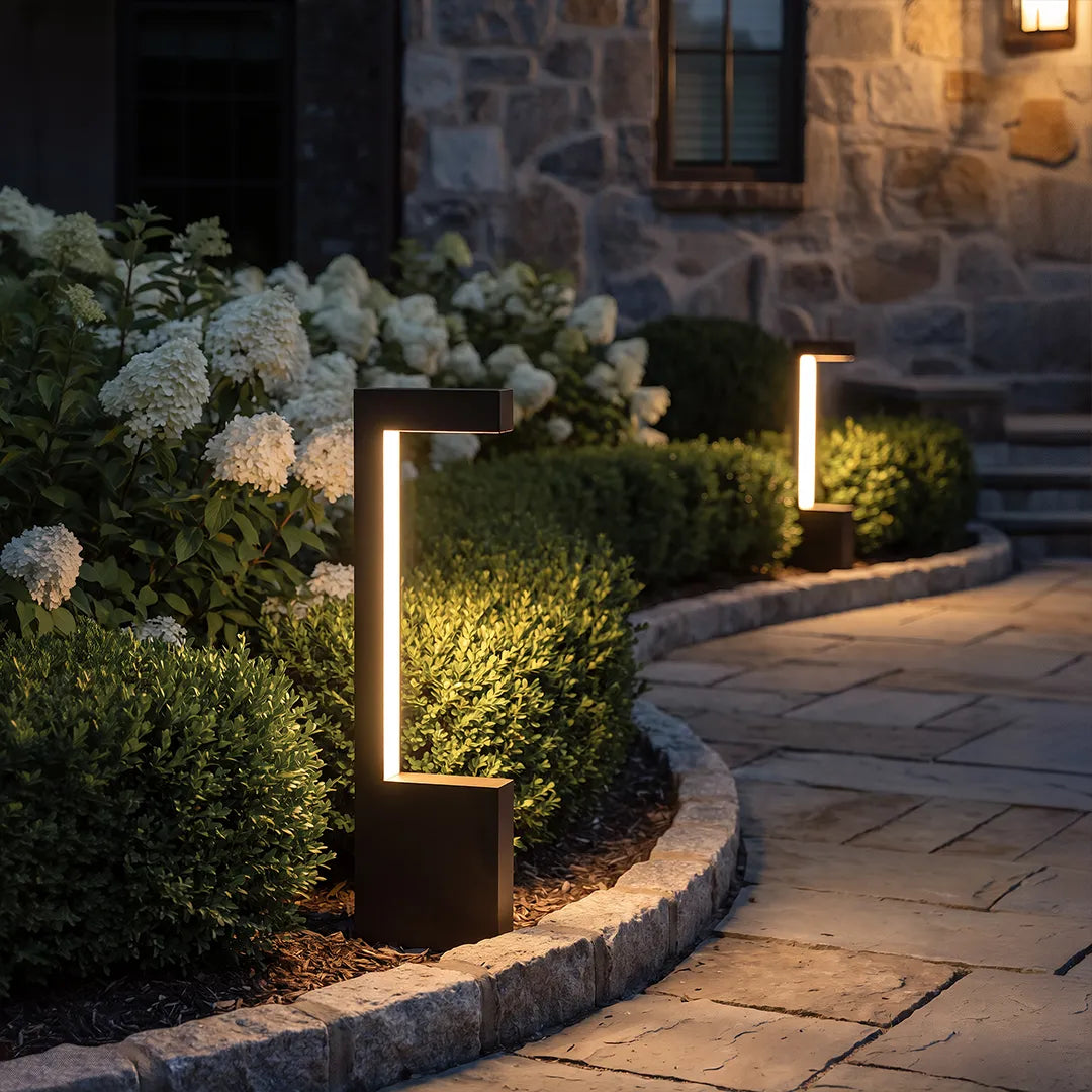 Modern LED bollard lights with warm glow along stone garden pathway and shrubs