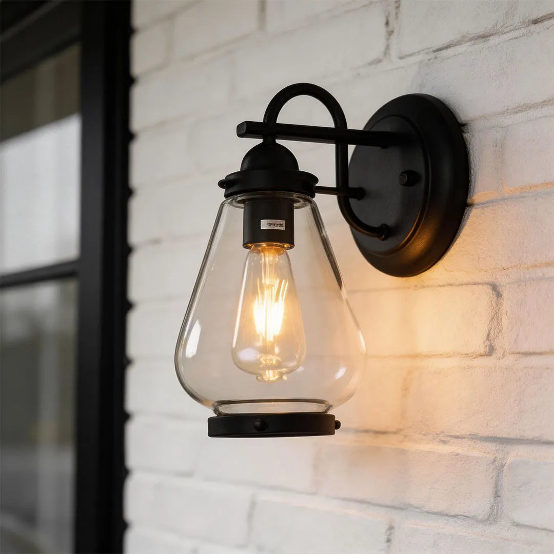 Modern LED outdoor wall light with black metal housing, clear textured glass, and warm downlight.