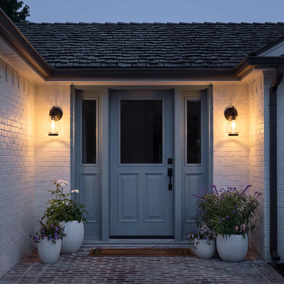 Modern LED outdoor wall light illuminating a textured exterior wall beside a landscaped walkway.