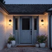 Modern LED outdoor wall light illuminating a textured exterior wall beside a landscaped walkway.