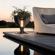 Modern lighted planter with a dark finish illuminating a poolside deck next to patio furniture at dusk.
