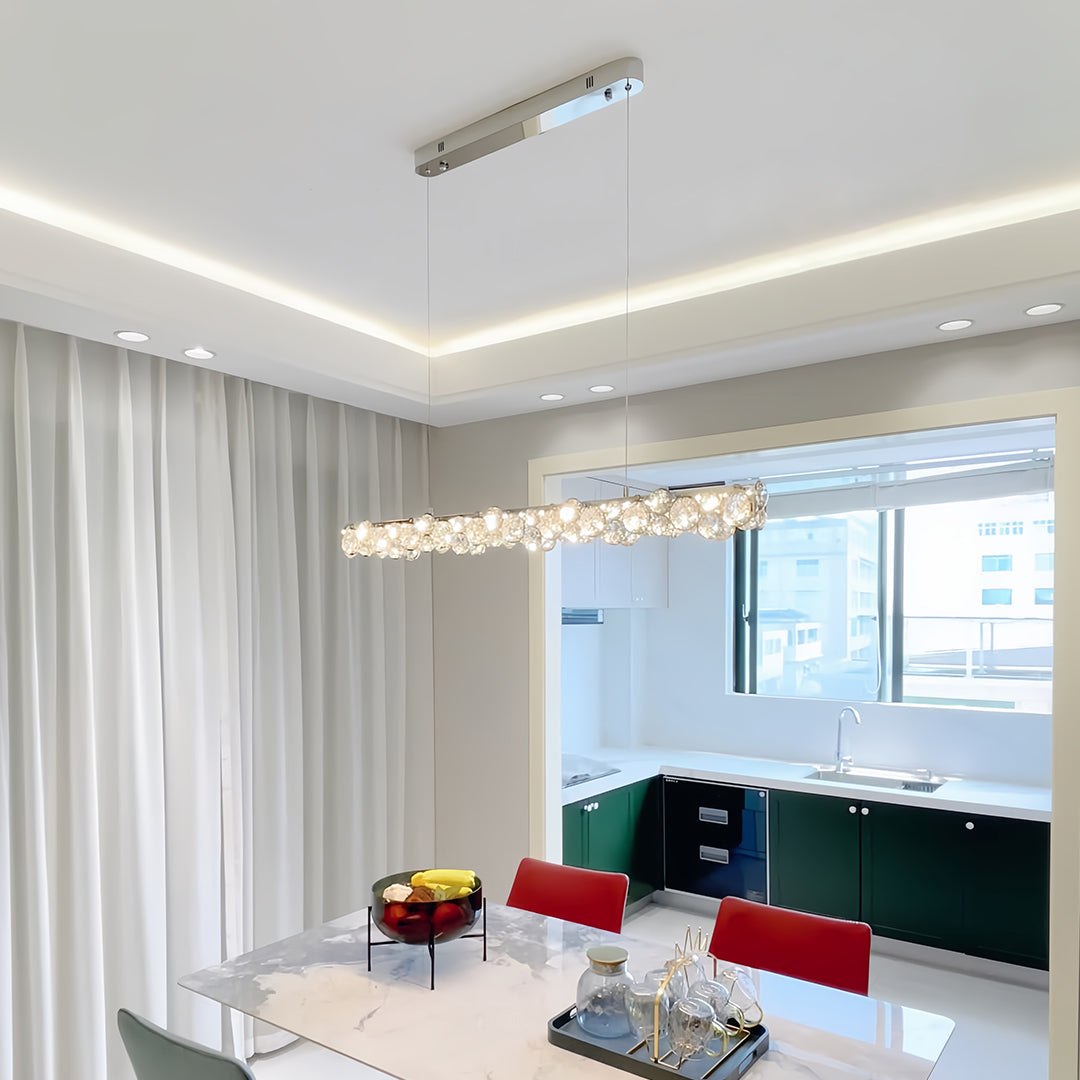 Modern silver pendant light featuring a long, linear design with multiple crystal orbs, hanging over a white dining table.