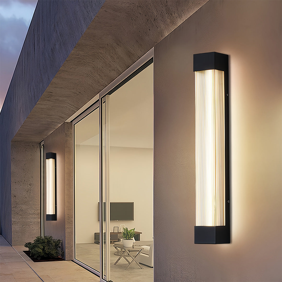 Modern linear outdoor sconce fixtures illuminating the exterior wall of a contemporary home with large glass doors.
