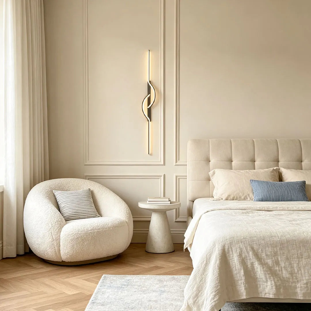Modern linear wall sconce installed next to a bed in a soft neutral bedroom with elegant wall paneling.