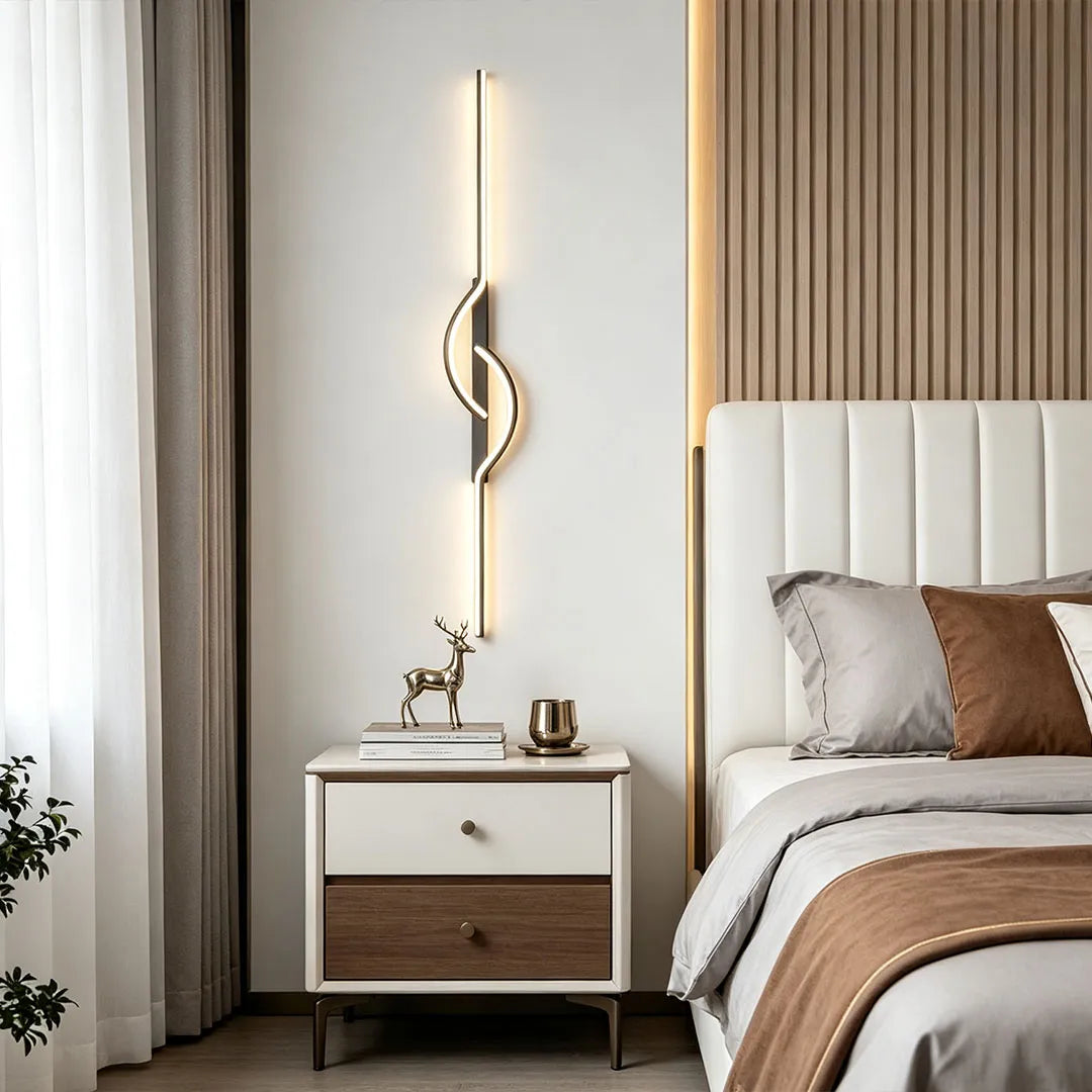 Modern linear wall sconce used as bedside lighting in a neutral bedroom with a nightstand and upholstered bed.