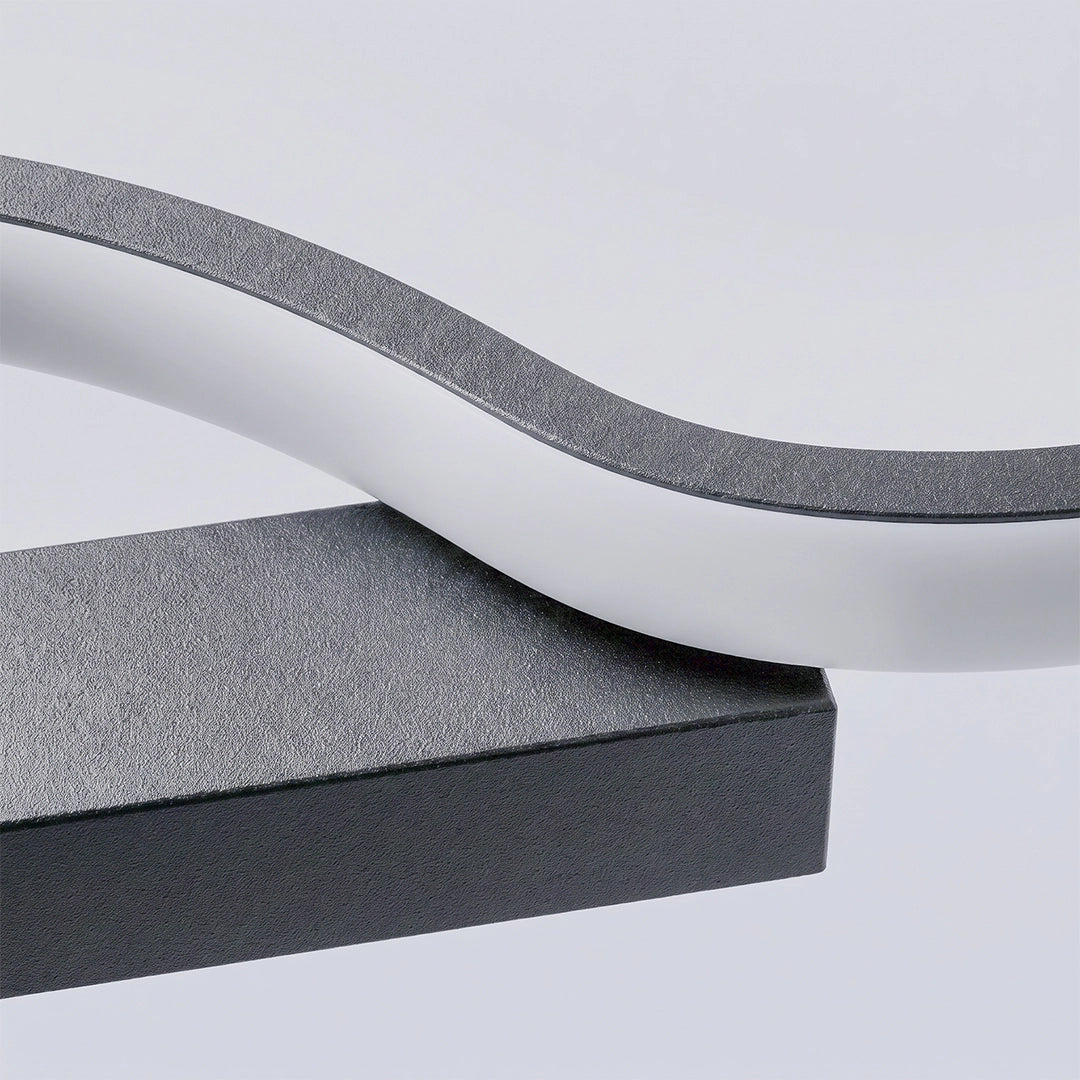 Close-up of the wavy white LED diffuser and textured black metal frame of a modern linear wall sconce.