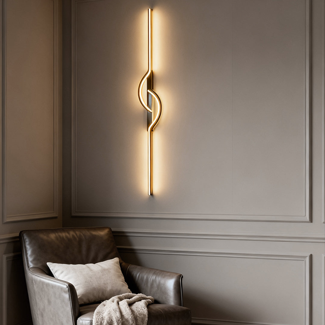 Vertical modern linear wall sconce with warm LED glow beside a contemporary armchair.