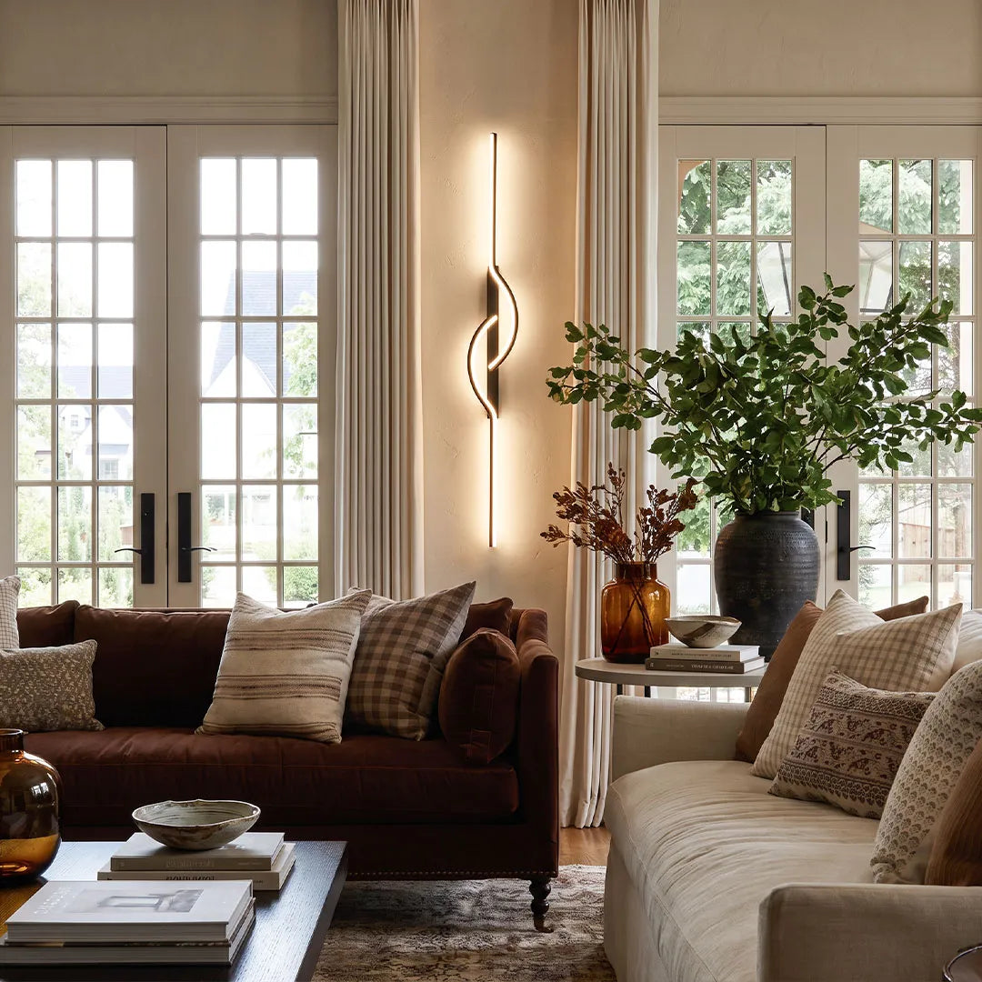 Modern linear wall sconce beside a sofa in a bright living room, adding warm vertical accent lighting.