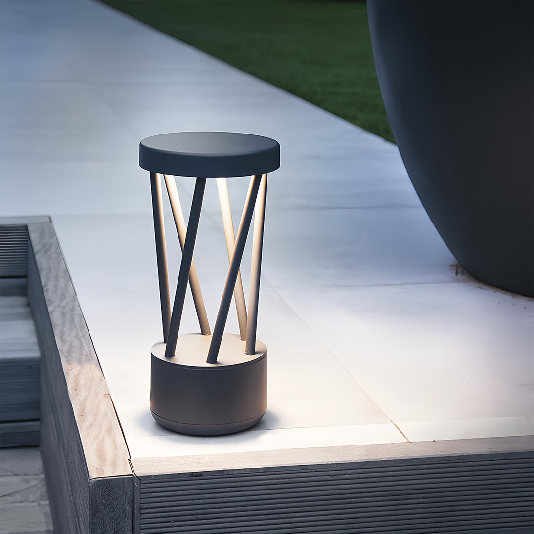 Line of modern black bright path lights with open metal cage top, illuminating a wooden and grass walkway at night.