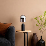 Modern minimalist black glass shade table lamp on an end table next to a dark sofa in a warmly decorated room. 