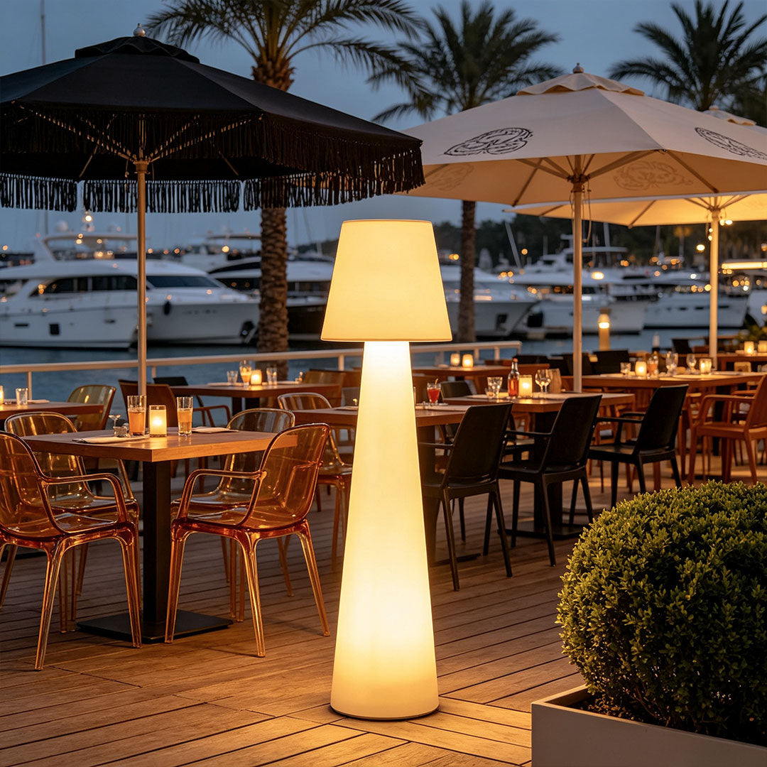 Modern minimalist floor lamp illuminating an outdoor restaurant terrace near a marina at night.