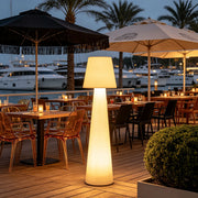 Modern minimalist floor lamp illuminating an outdoor restaurant terrace near a marina at night.