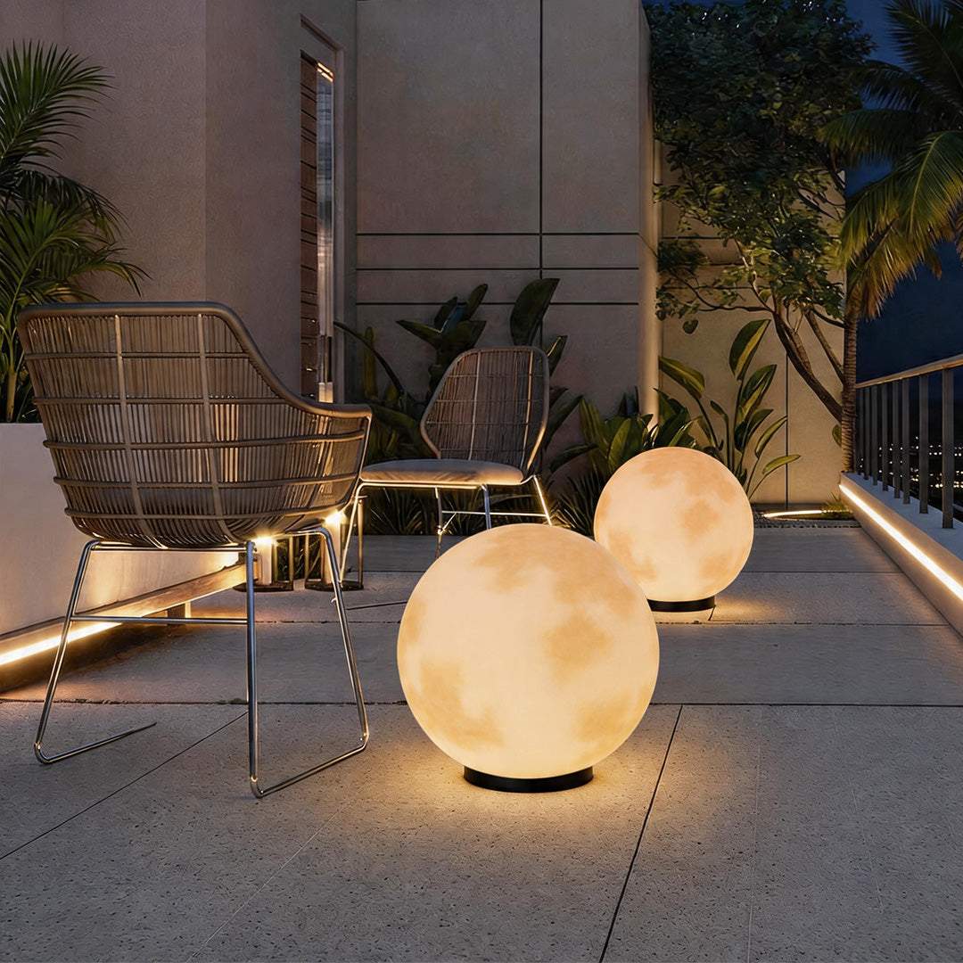 Modern moon pillar lights glowing on a stone patio floor next to elegant outdoor lounge chairs.