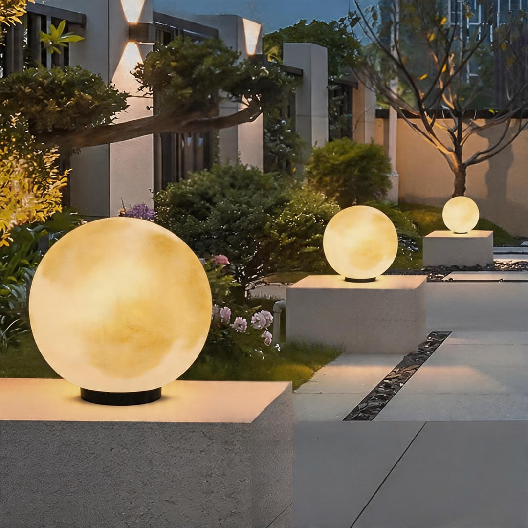 Modern moon pillar lights glowing on stone pedestals along a beautiful garden pathway at dusk.