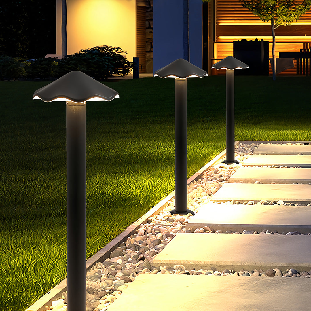 Modern black metal pathway lights with mushroom cap design, illuminating a stone path beside a grassy lawn at night.