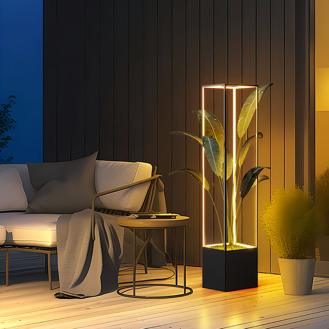 Modern outdoor square floor lamps with a sleek black base and illuminated vertical frame, holding a potted plant on a patio setting.