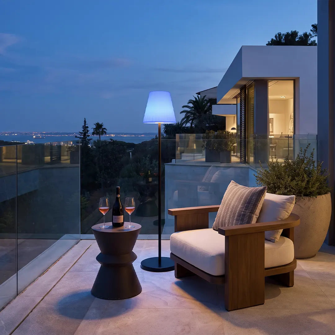 Modern outdoor floor lamp lighting a contemporary terrace next to cushioned outdoor seating at dusk.