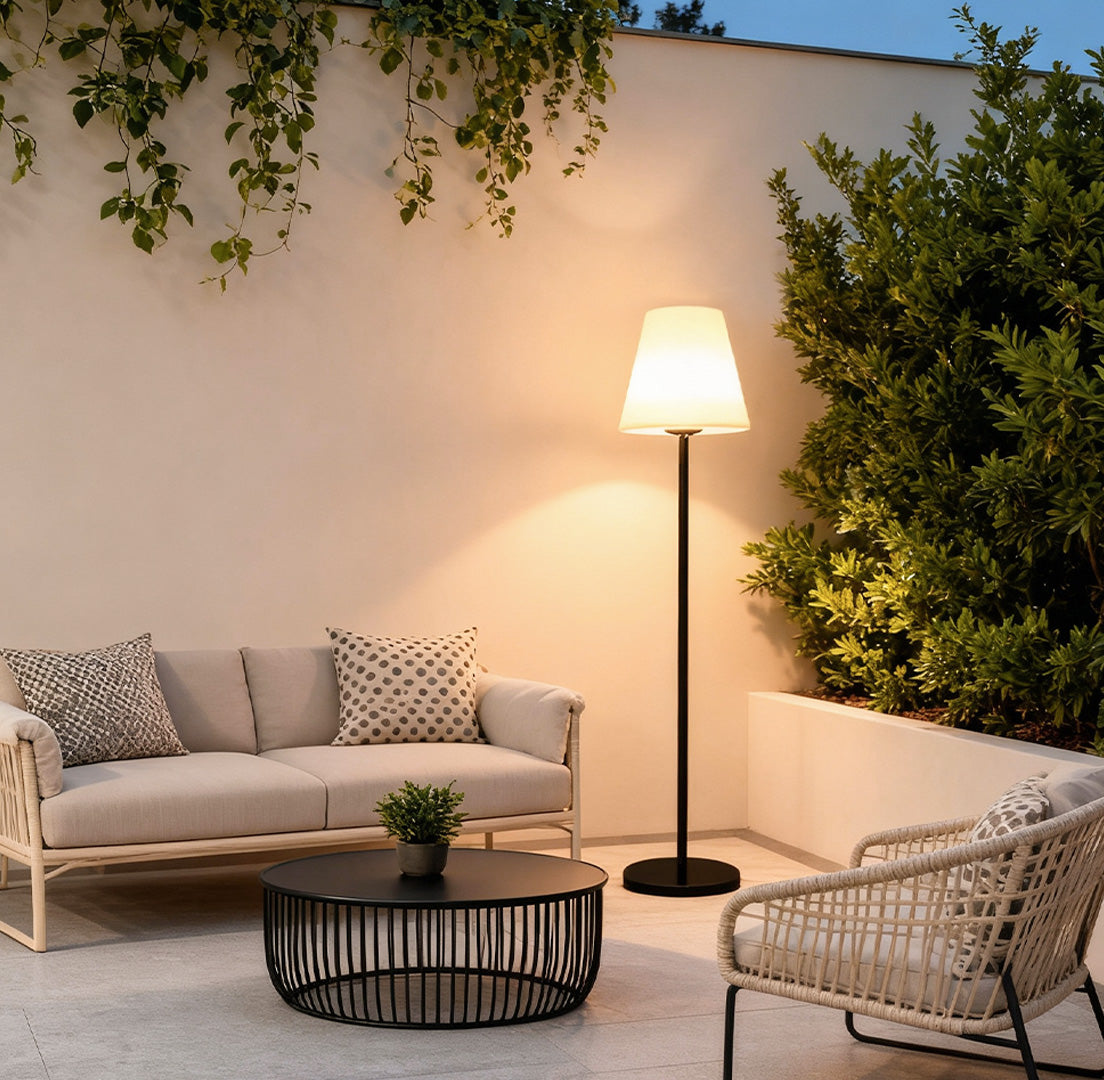 Modern outdoor floor lamp illuminating a cozy patio seating area with wicker furniture and greenery.