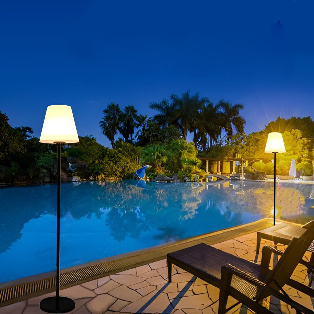 Modern outdoor floor lamps standing by a pool, casting a soft glow over the evening water.