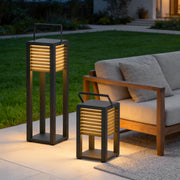 Modern outdoor floor lantern placed beside patio seating with warm ambient lighting.