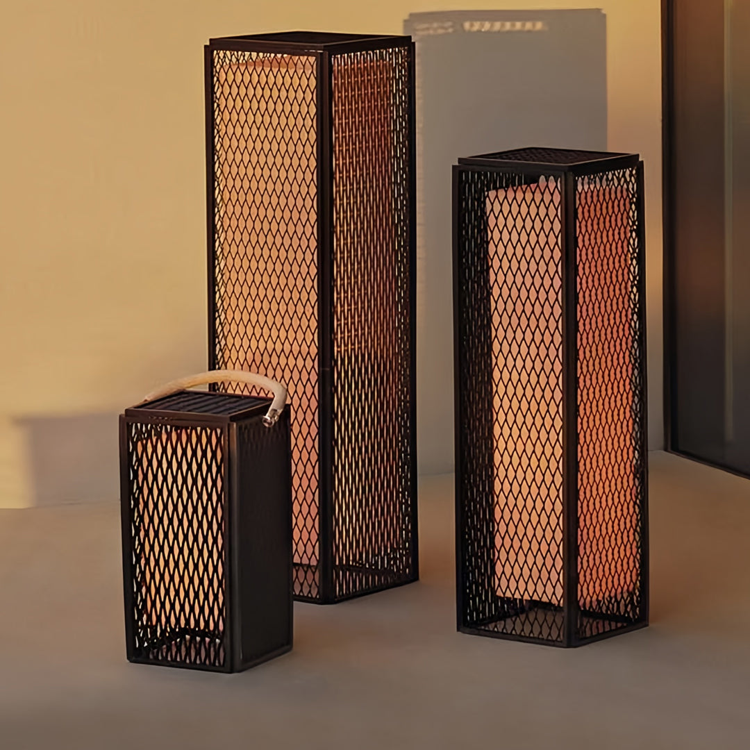 Grouping of modern outdoor lanterns on a patio with warm mesh lighting and modern architectural backdrop.