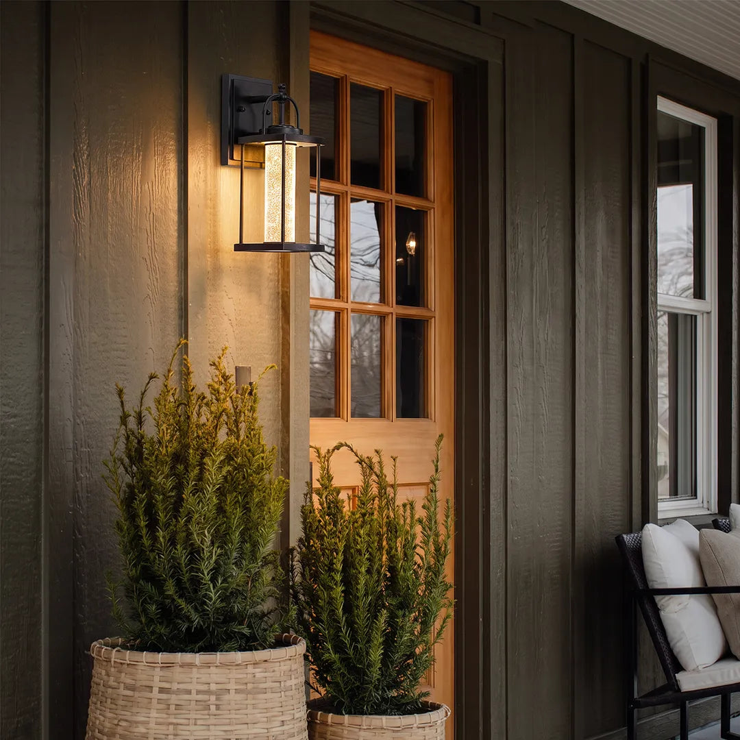 Modern outdoor lantern wall sconce beside a front door with dark siding and warm ambient lighting.