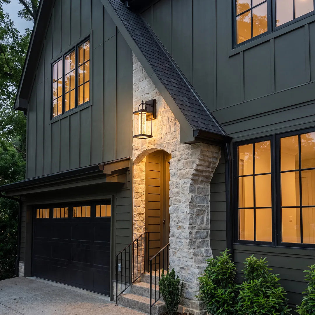Modern outdoor lantern wall sconce illuminating a two-story home entry with stone accents and dark siding.