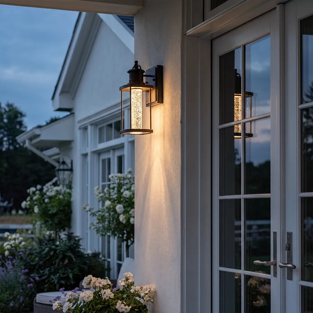 Modern outdoor lantern wall sconce installed beside a patio door on a white exterior wall at dusk.