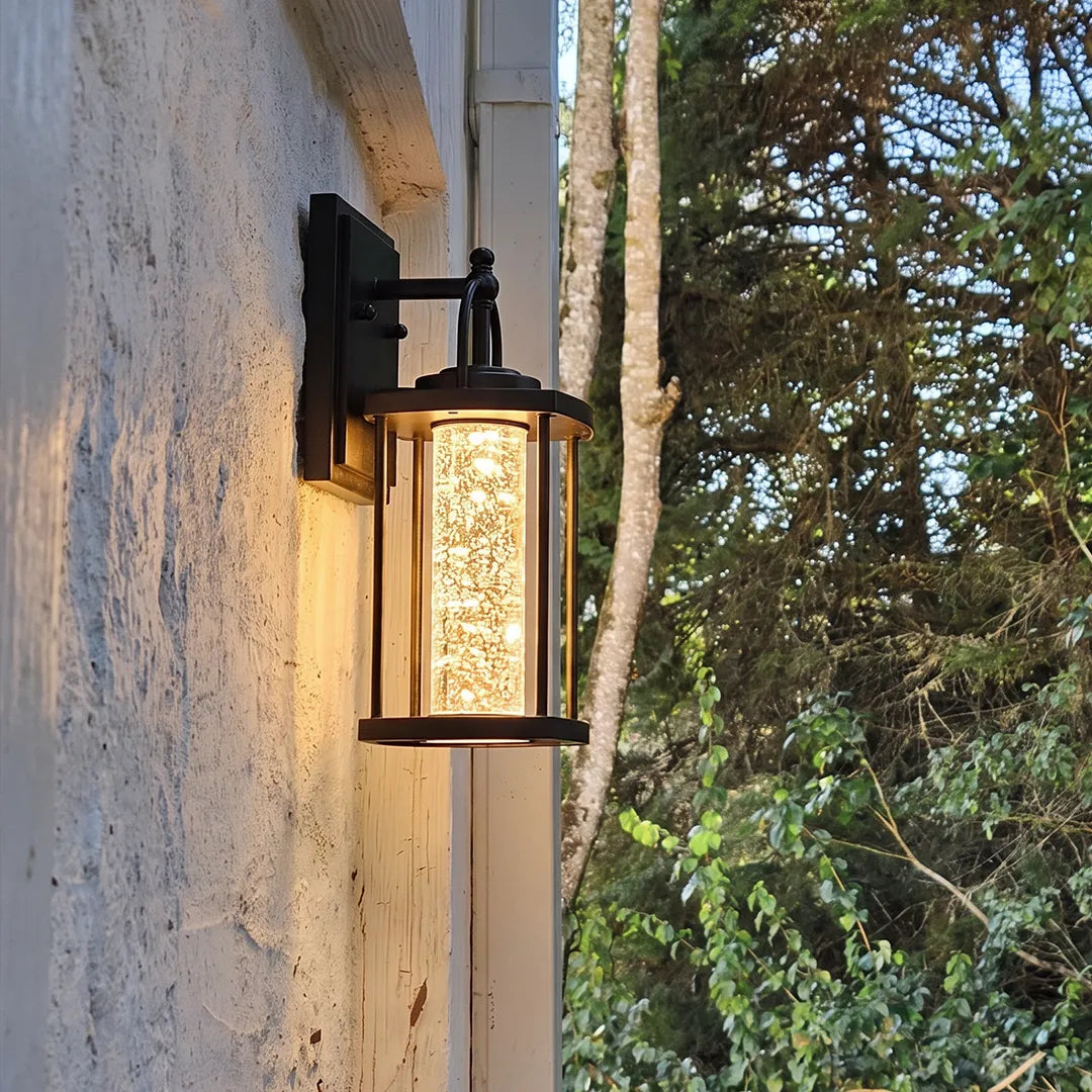 Modern outdoor lantern wall sconce with clear seeded glass mounted on a light stucco exterior wall.