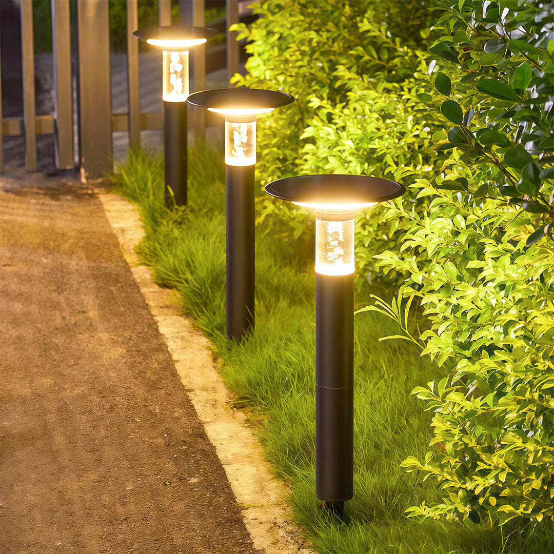 Modern outdoor path lights solar powered, lining a walkway and garden bed with warm light.