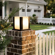 Modern outdoor pillar light with warm glow on brick column beside white picket fence