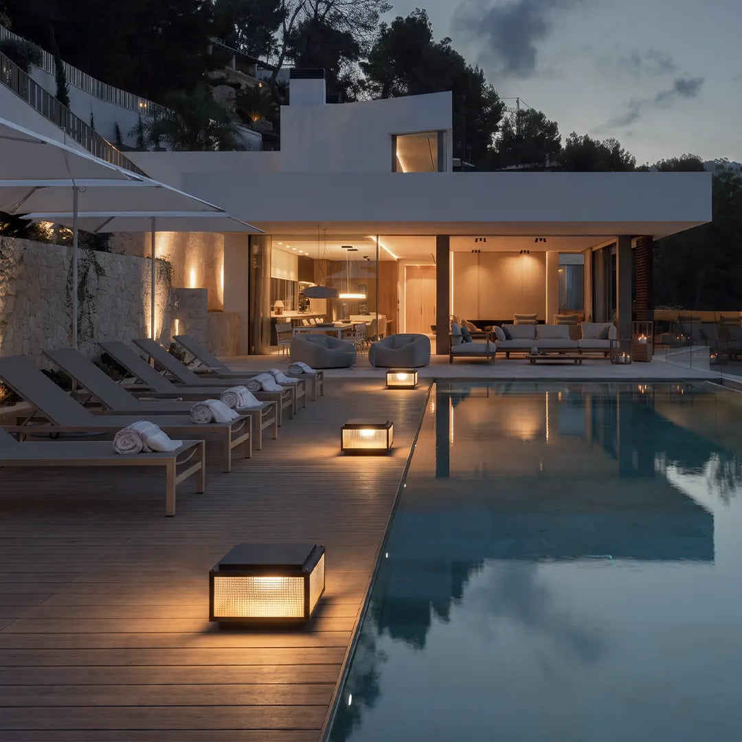 Modern outdoor pillar light fixtures placed around a luxury poolside patio and walkway at night.