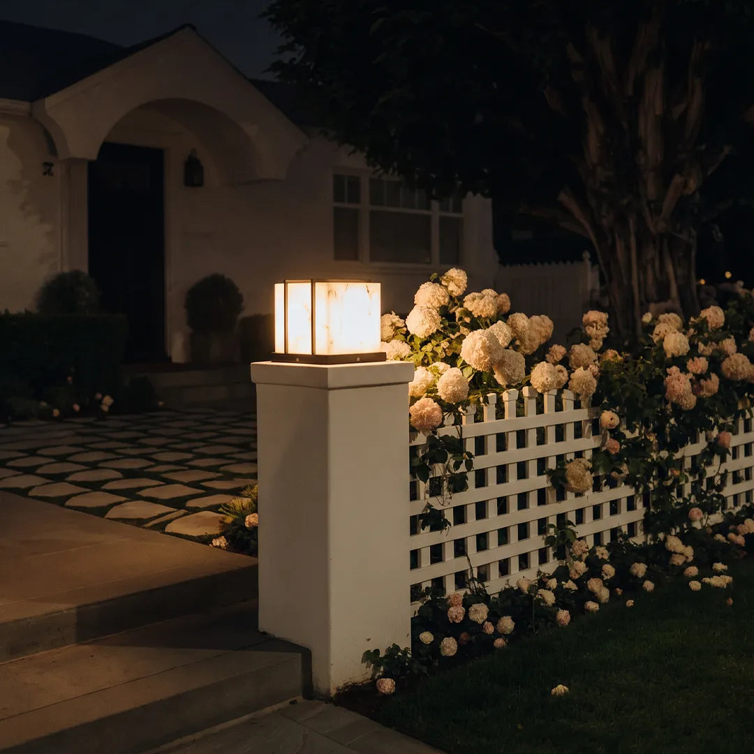Modern outdoor pillar light on white garden column beside flowers and fence