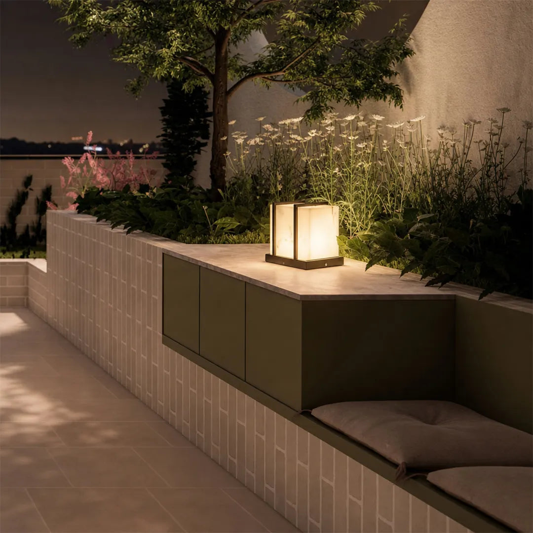 Modern outdoor pillar light with warm glow on terrace wall beside garden plants