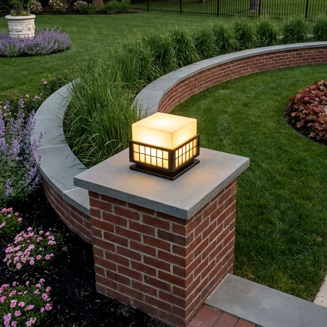 Modern outdoor pillar lights installed on a brick pillar beside a landscaped garden walkway.