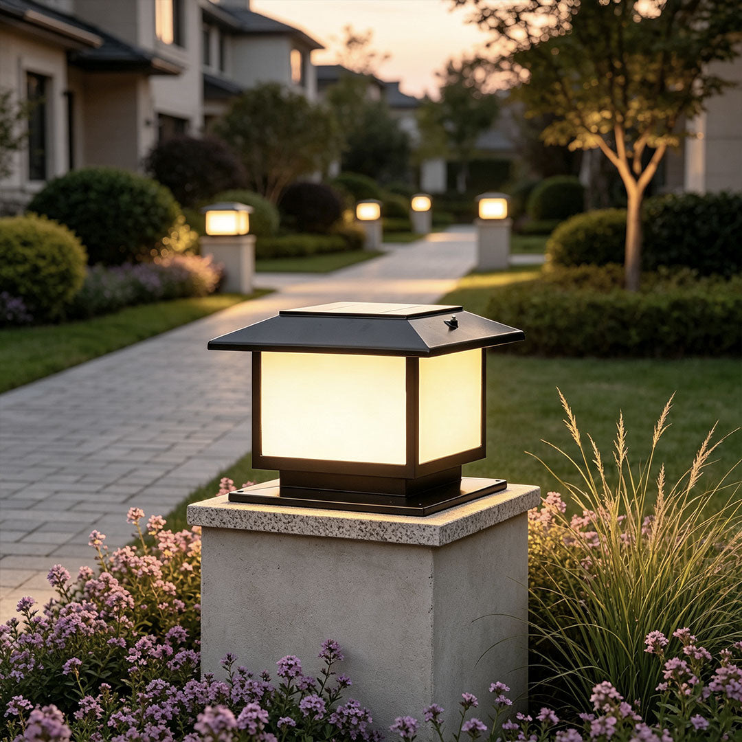 Modern outdoor pillar lights mounted on a concrete gate post beside a landscaped walkway at dusk.