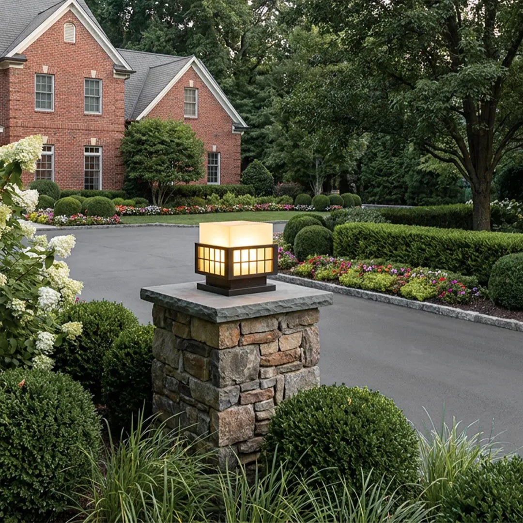 Modern outdoor pillar lights installed on stone columns beside a residential driveway.