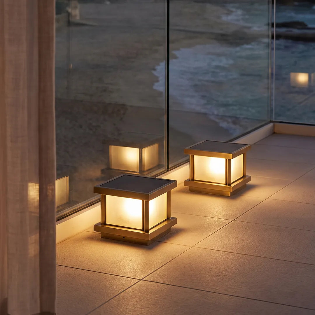 Modern outdoor pillar lights with warm glow beside glass wall and patio