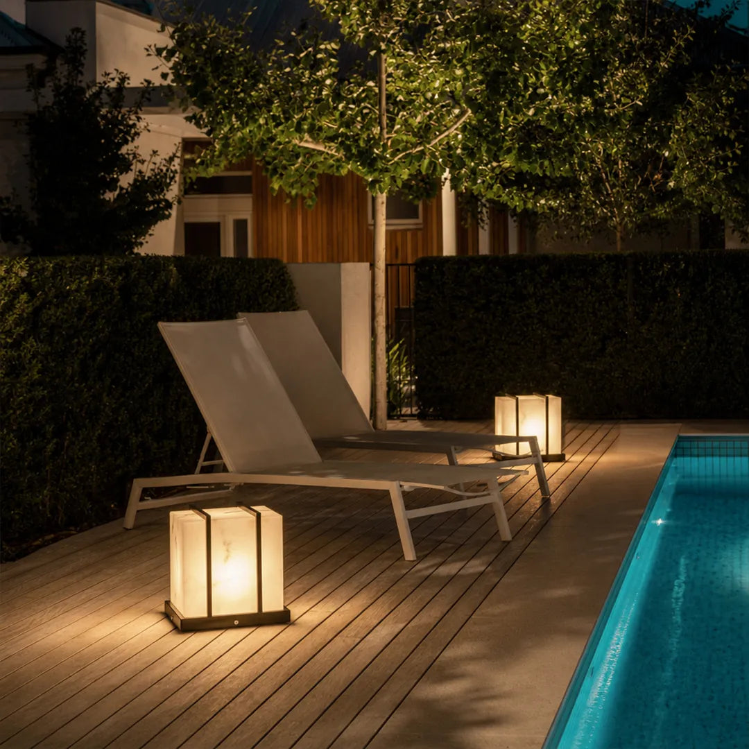 Modern outdoor pillar lights illuminating poolside deck and lounge chairs