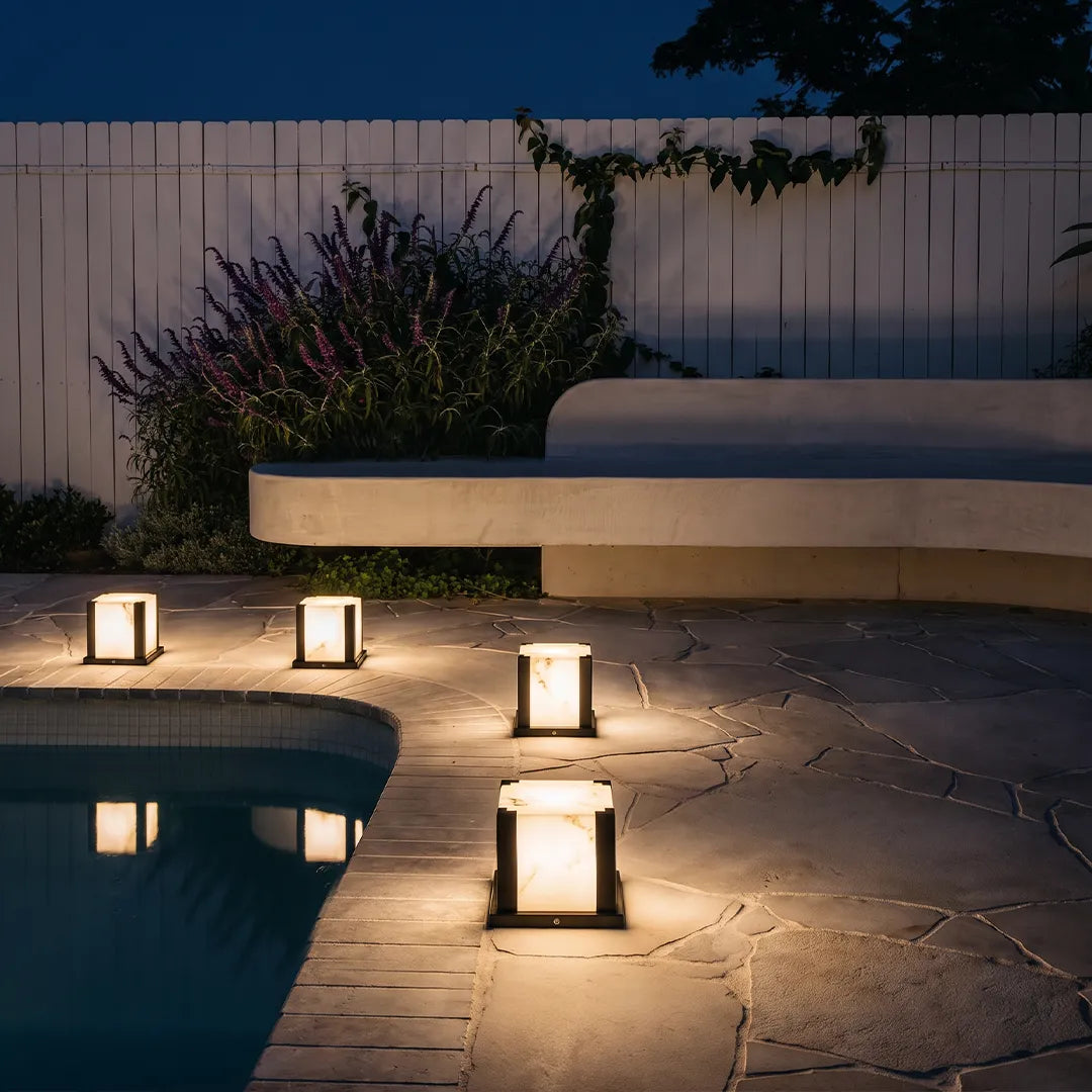 Modern outdoor pillar lights illuminating poolside patio and garden at night
