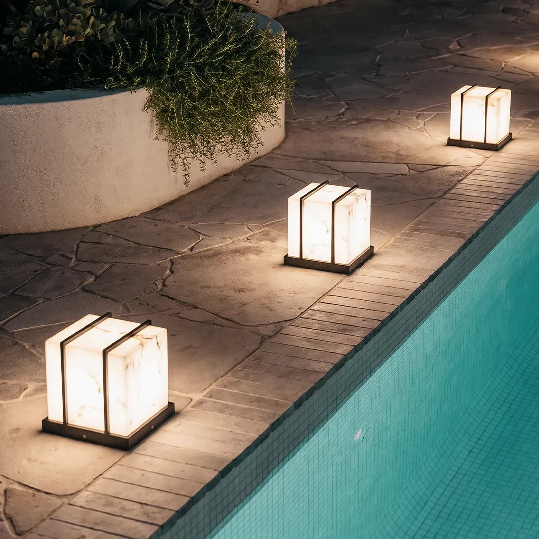 Modern outdoor pillar lights with warm glow along stone poolside walkway