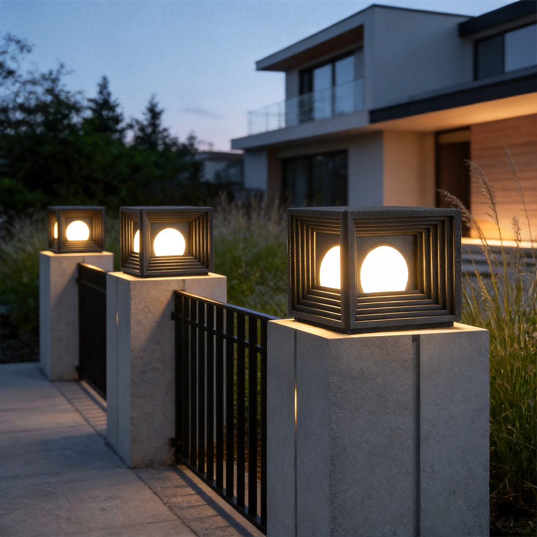 Modern outdoor pillar lights with a sleek black finish, enhancing a garden fence at night.