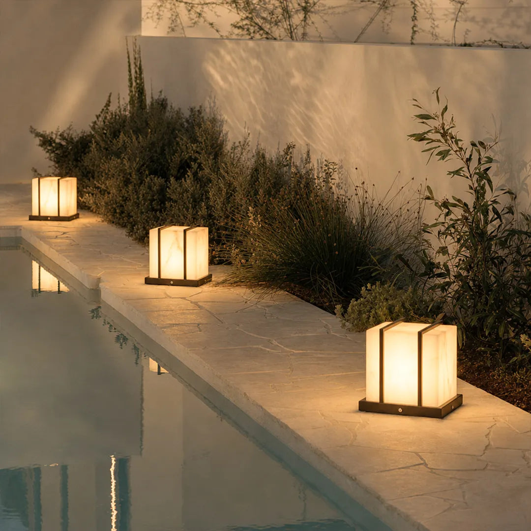 Modern outdoor pillar lights with warm glow beside swimming pool and garden